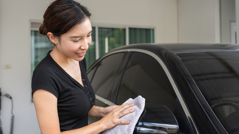 A woman in a black top cleaning a black vehicle with a microfiber cloth.
