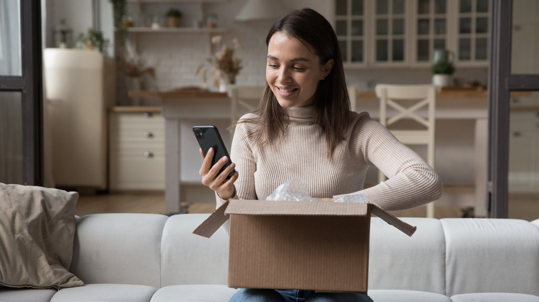 A woman checking her iPhone with one hand and a courier box with the other hand.