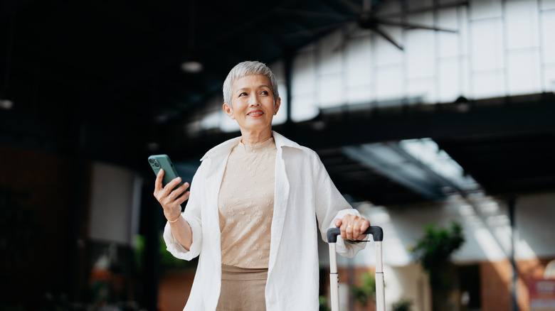 older woman using iPhone while holding luggage