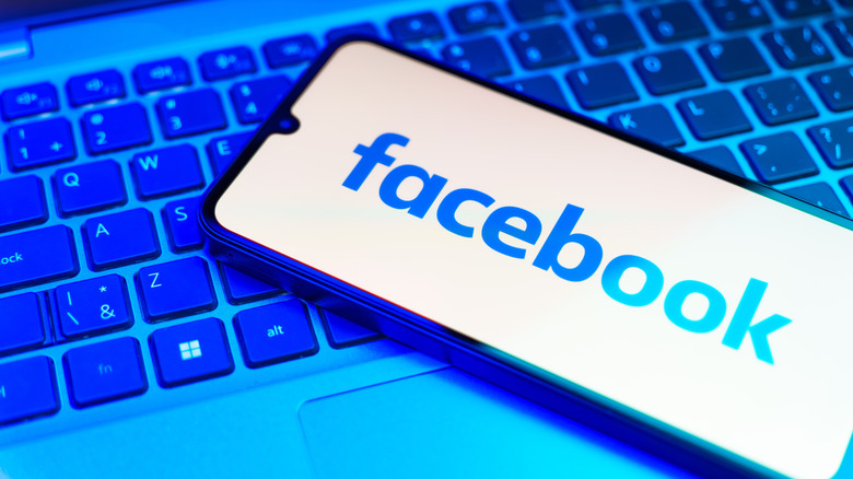 Smartphone on a laptop keyboard showing the Facebook logo