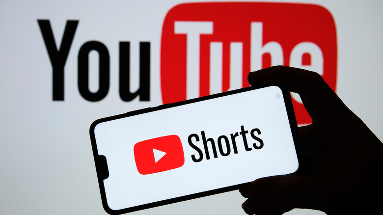 Shorts on phone, YouTube logo in background