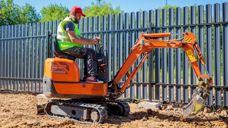 orange mini excavator by fence