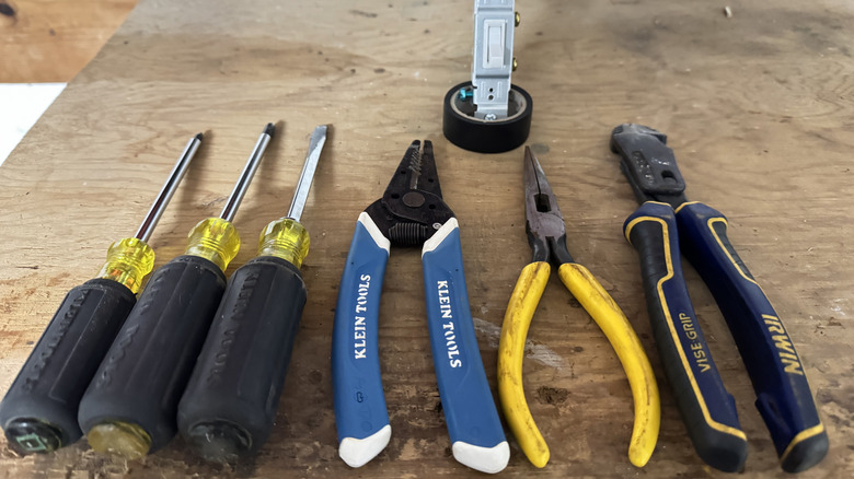 A close up shot of hand tools and a light switch on a workbench