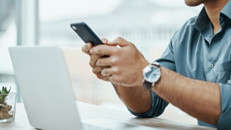 man holding phone in front of laptop