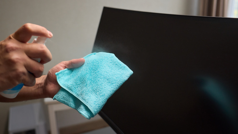 Hand spraying water on microfiber cloth with curved screen in the background
