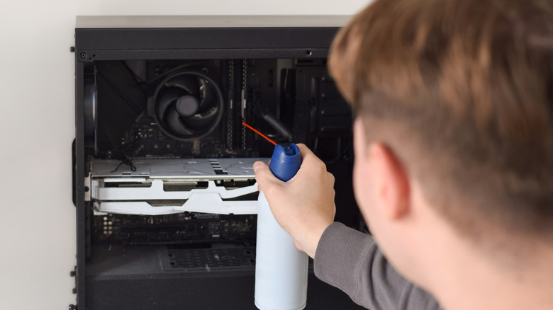 Young man cleaning the inside of a computer with compressed air duster