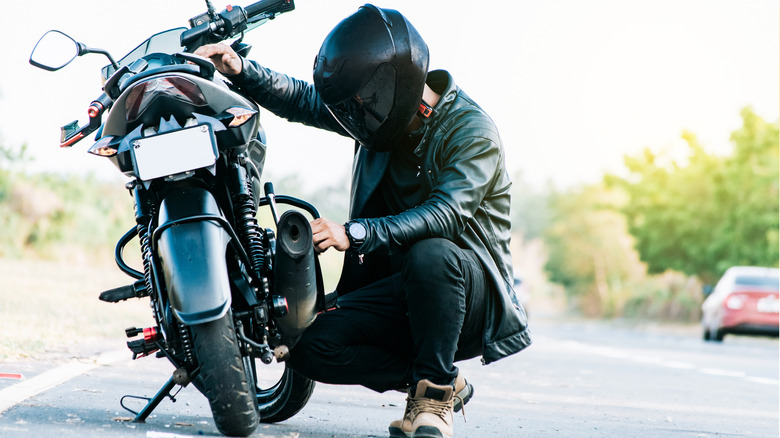 Motorcyclist inspects bike on side of road