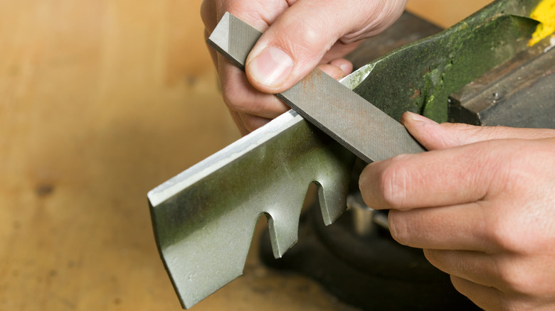 A person sharpening a lawn mower blade.