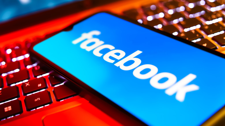Smartphone on a laptop keyboard showing Facebook logo.