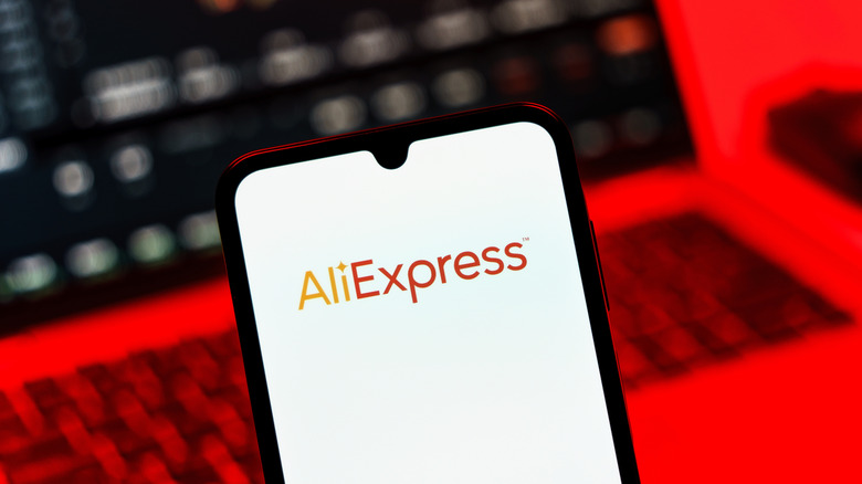 A phone with AliExpress logo and laptop in background