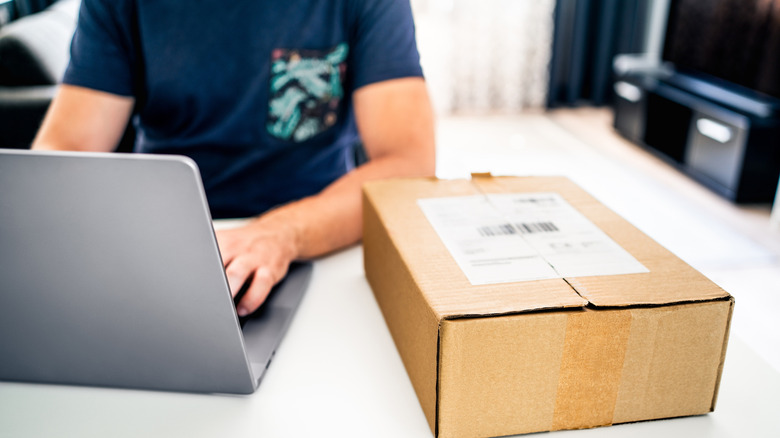 A person working on a laptop with deivery package kept on the side