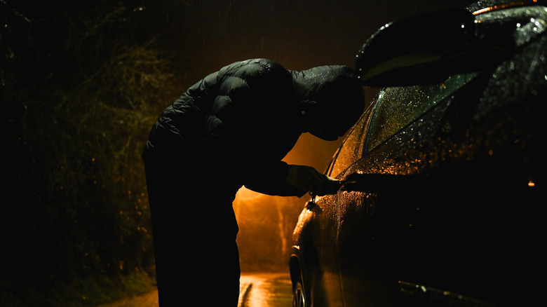 A thief wearing hood trying to steal a car at night