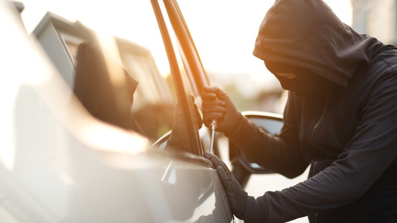 A thief trying to open a car's window to steal the vehicle