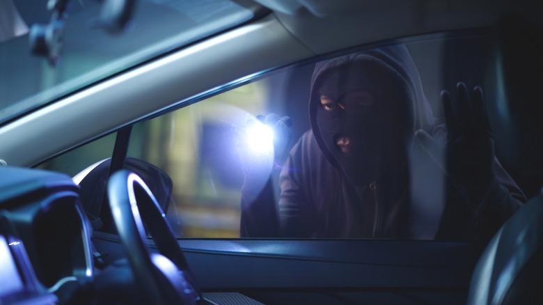 A thief looking inside a car using a torch