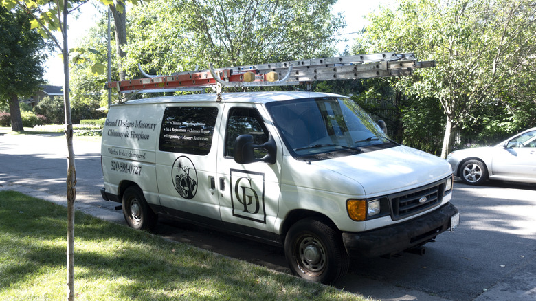 White van with business information stenciled on the side and a ladder mounted to the roof