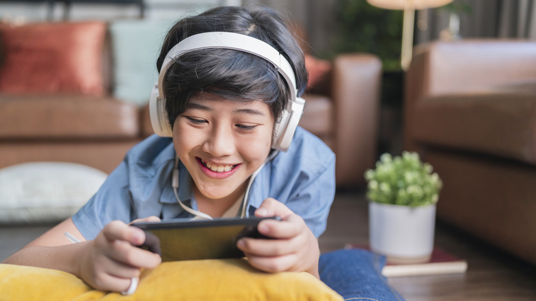 Child wearing headphones, holding and smiling at smartphone