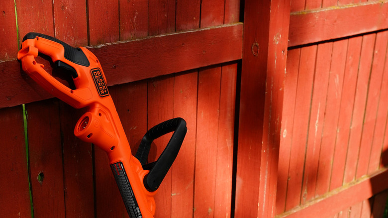Close-up of a Black+Decker weed eater leaning against a red fence