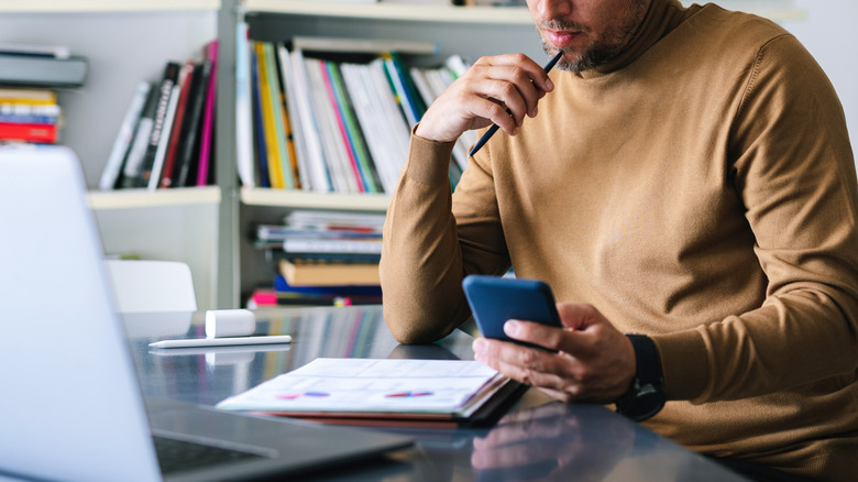 man looking at notes holding phone