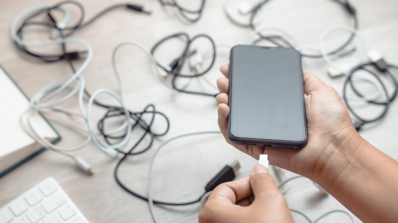 Connecting a cable to a phone with a mess of other cables in the background