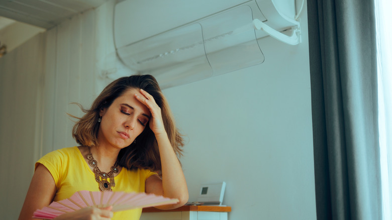 A woman fanning herself under a broken AC unit
