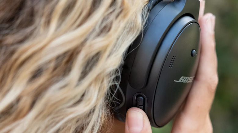 A person is pressing the button on her Bose QuietComfort 45 headphones