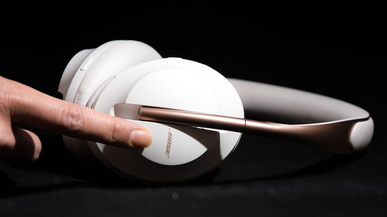 A person has their finger on a pair of white Bose Noise Cancelling Headphones 700