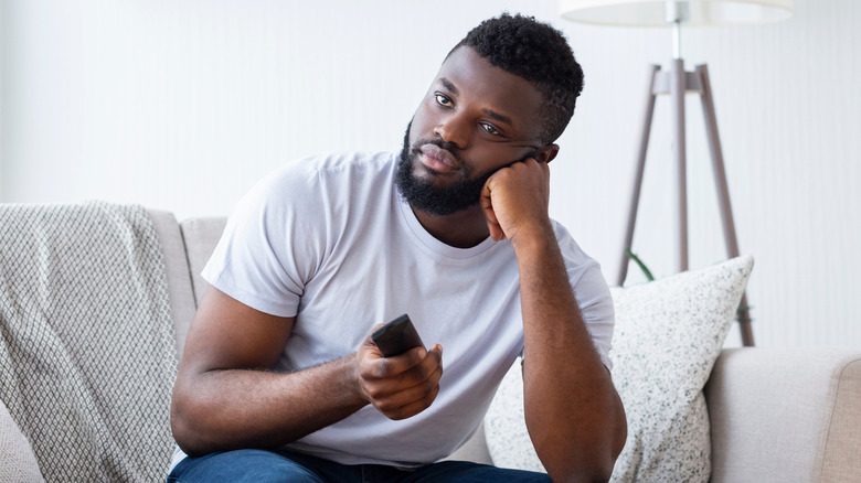 person sitting on couch, remote in hand, looking annoyed while looking at TV