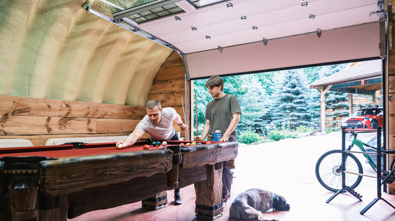 Two young man playing pool inside a garage that has been transformed into a man cave