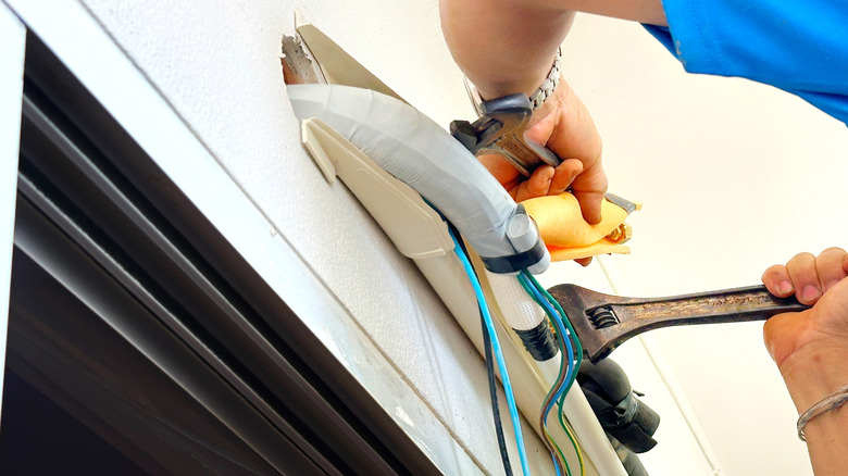The hands of an air conditioner technician holding a screwdriver or tool to install and assemble the air conditioner drain pipe.