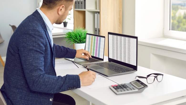 man maintaining spreadsheets on multiple laptops