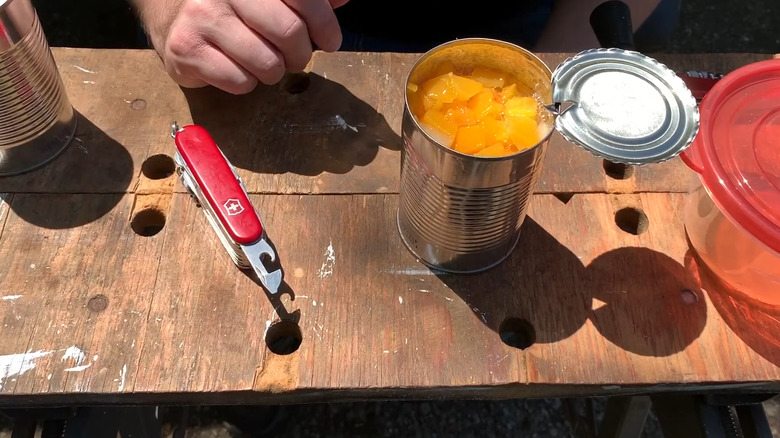 Swiss Army Knife with can opener tool exposed next to open can of fruit on wooden table