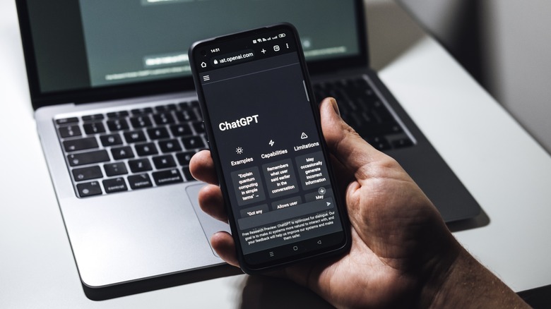 ChatGPT on smartphone screen laptop behind
