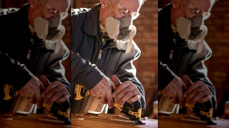 A man wearing safety glasses and a dust-filter facemask while using a DeWalt oscillating multi-tool.