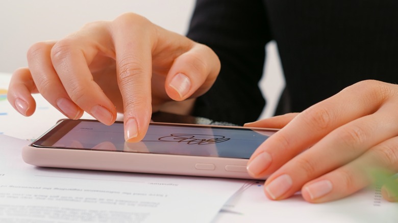 Hands drawing out a digital signature on a smartphone