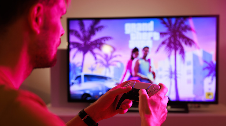 man with playstation controller looks at grand theft auto 6 logo on tv