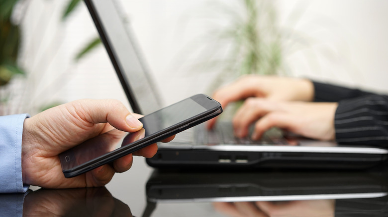 hand on phone and another hand on laptop