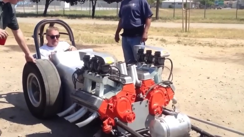 Twin-engine dragster parked with driver inside, front-right view