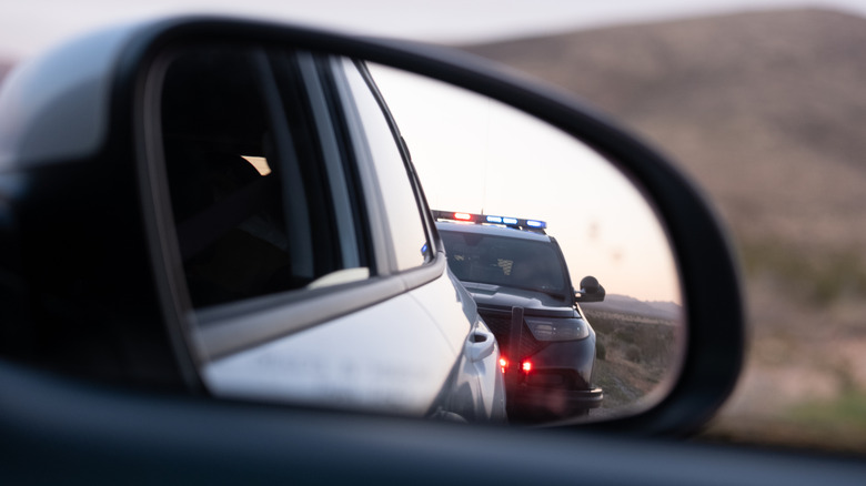 Close-up of a police vehicle approaching in a rear view mirror.