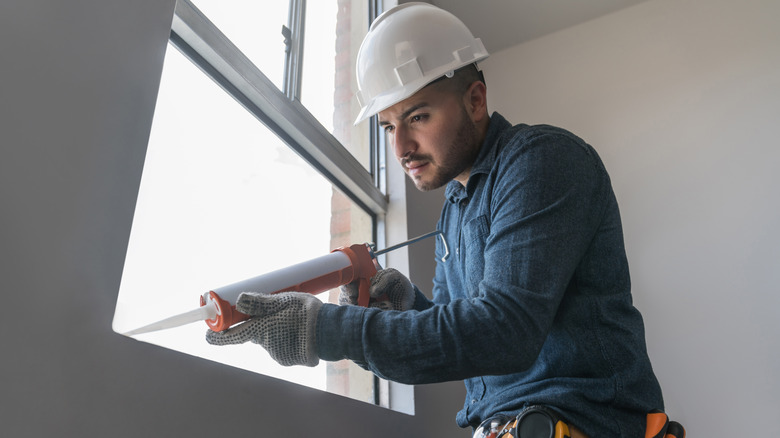 A person using a caulking gun on a window.