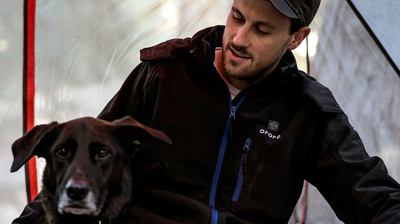 Man in tent wears black Ororo jacket with dog