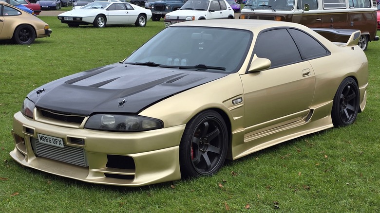 Gold modified Nissan Skyline R33 GT-R parked on grass at a car show