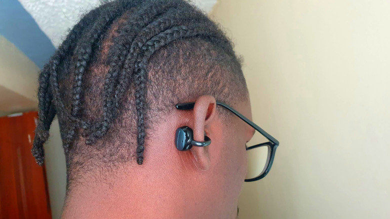 Man wearing glasses and clip-on earbuds seen from behind.