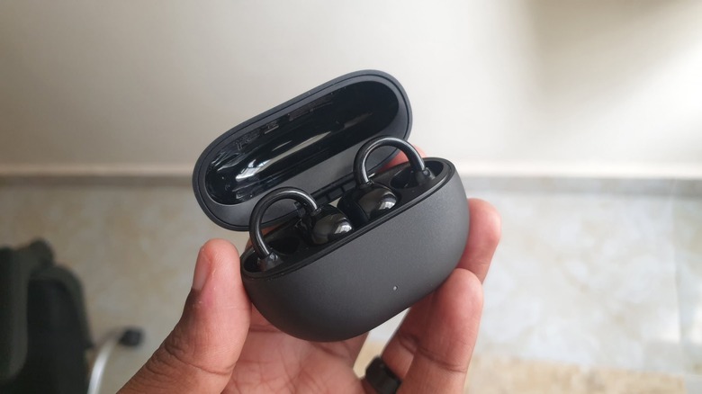 Person holding an open case of clip-on earbuds.