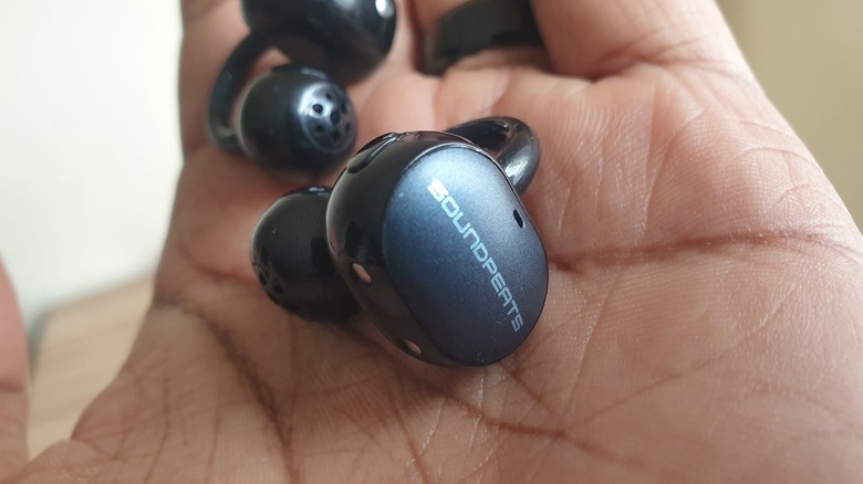 A pair of soundpeats clip-on earbuds in hand.