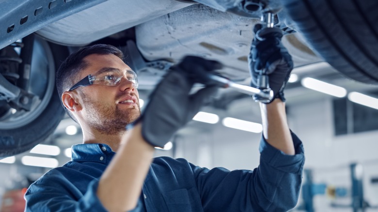 Mechanic using ratchet on car undercarriage