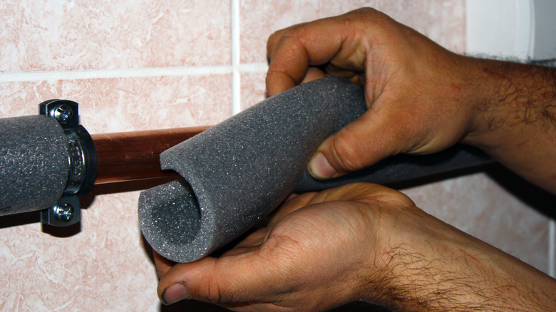 A person installing foam insulation on a pipe