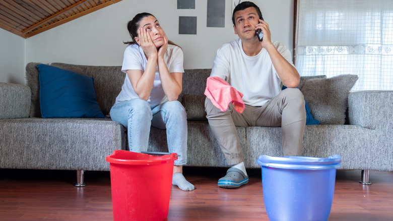 A distressed couple attempting to call a professional to sort out a home issue, a blue and a red bucket in front of them
