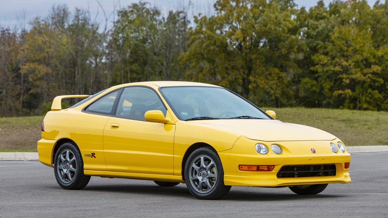 Yellow 2001 Acura Integra Type R parked in front of woods in parking lot, front-right 3/4 view