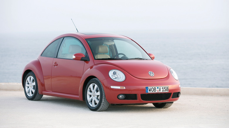 A red facelift Volkswagen New Beetle next to a coast, front 3/4 view