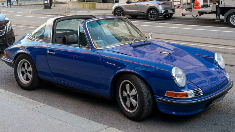 A blue Porsche 911 convertible parked by the sidewalk